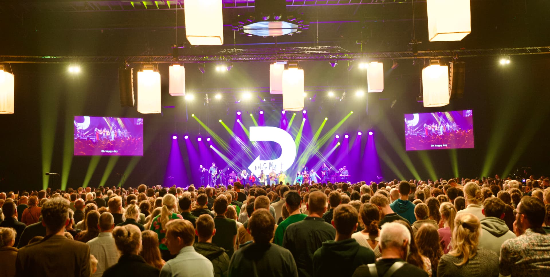 Grote zaal met paarse lichten en publiek
